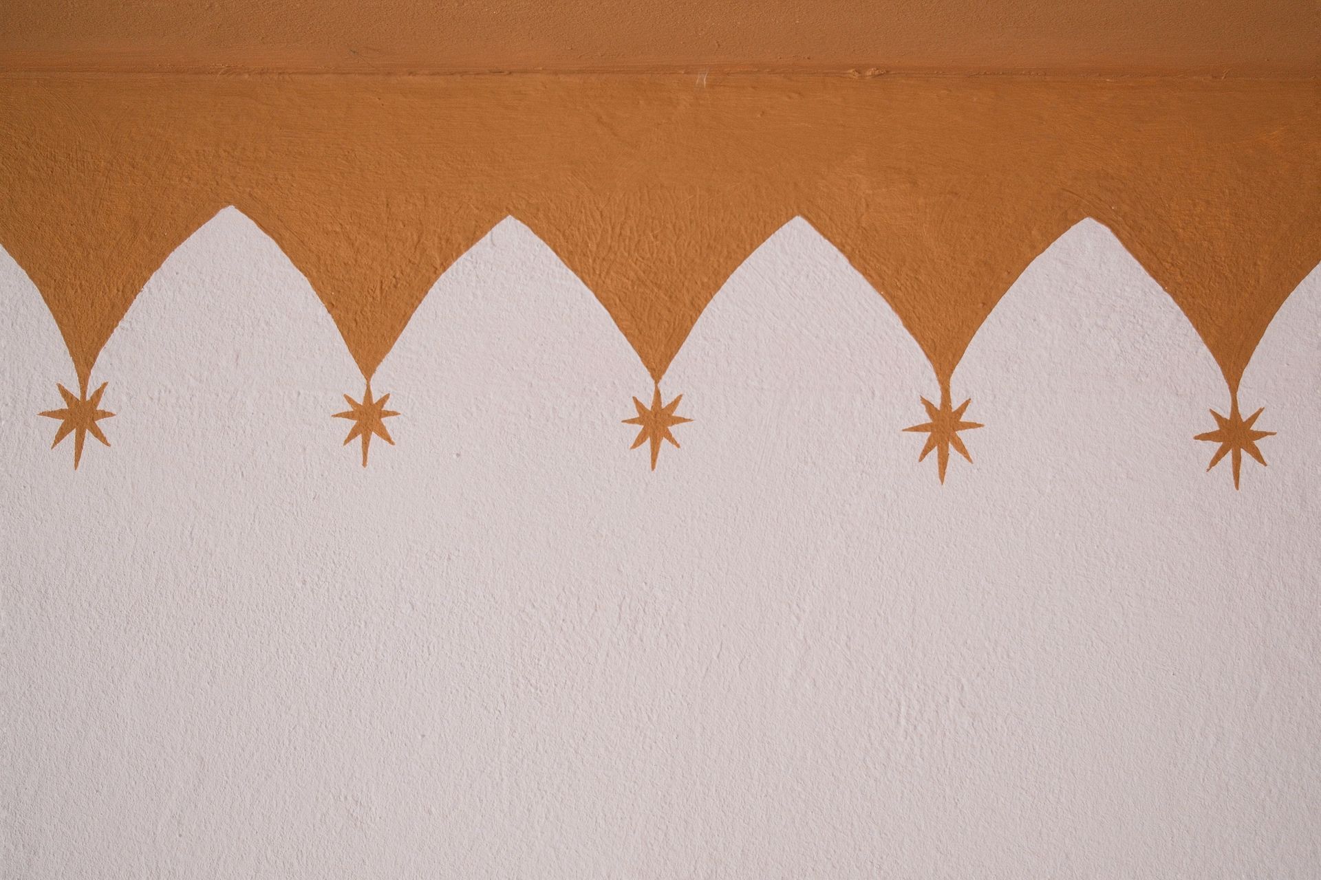 A textured, white wall features a decorative brown border with a repeated pointed arch pattern and hanging star icons.
