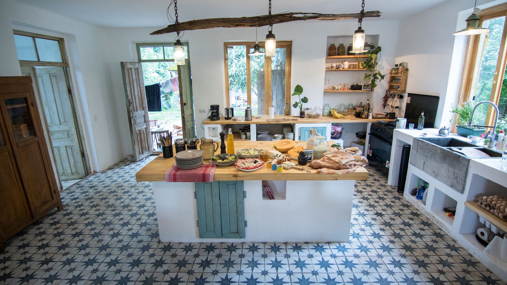 A rustic kitchen with blue and white patterned tile floors, a central wooden island, and white counters.