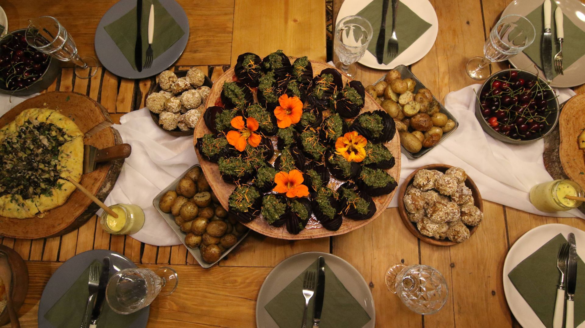 A top-down view of a rustic wooden dining table set with various plates of food, including toasted bread and small fruit.