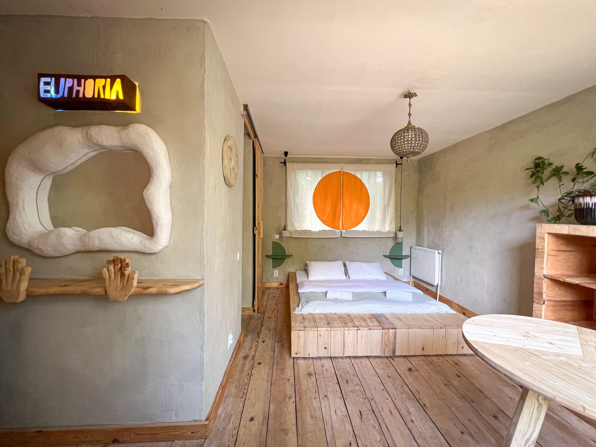 A bedroom with light wood floors, a platform bed, a sun-shaped window design, and a neon