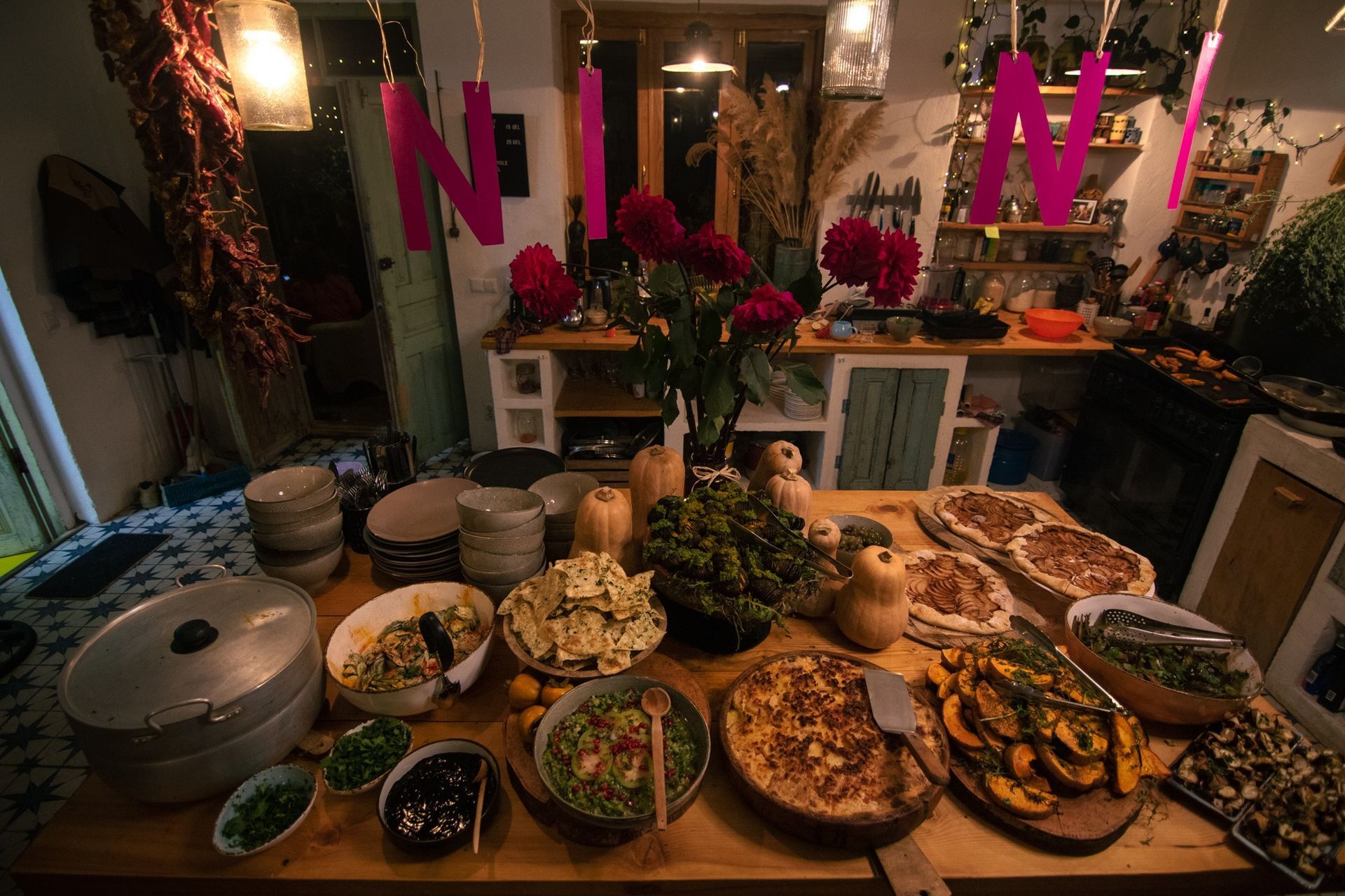 A table laden with various prepared dishes, salads, and baked goods in a cozy, decorated home kitchen.
