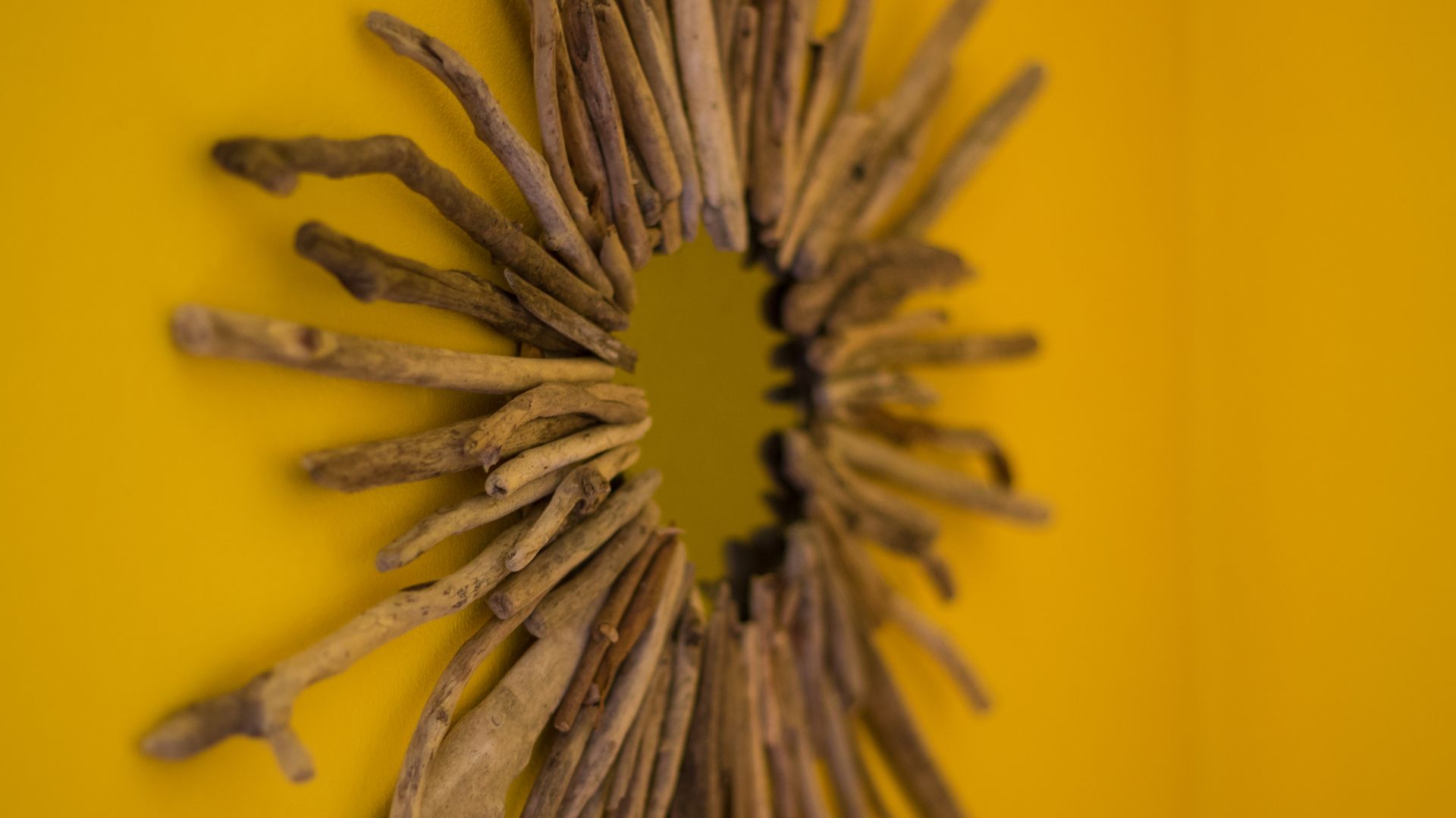 A sunburst-style wall mirror decorated with radiating pieces of driftwood mounted on a bright yellow wall.