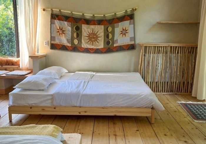 A rustic bedroom featuring a platform bed with white bedding, a sun-themed wall tapestry, and light wood flooring.