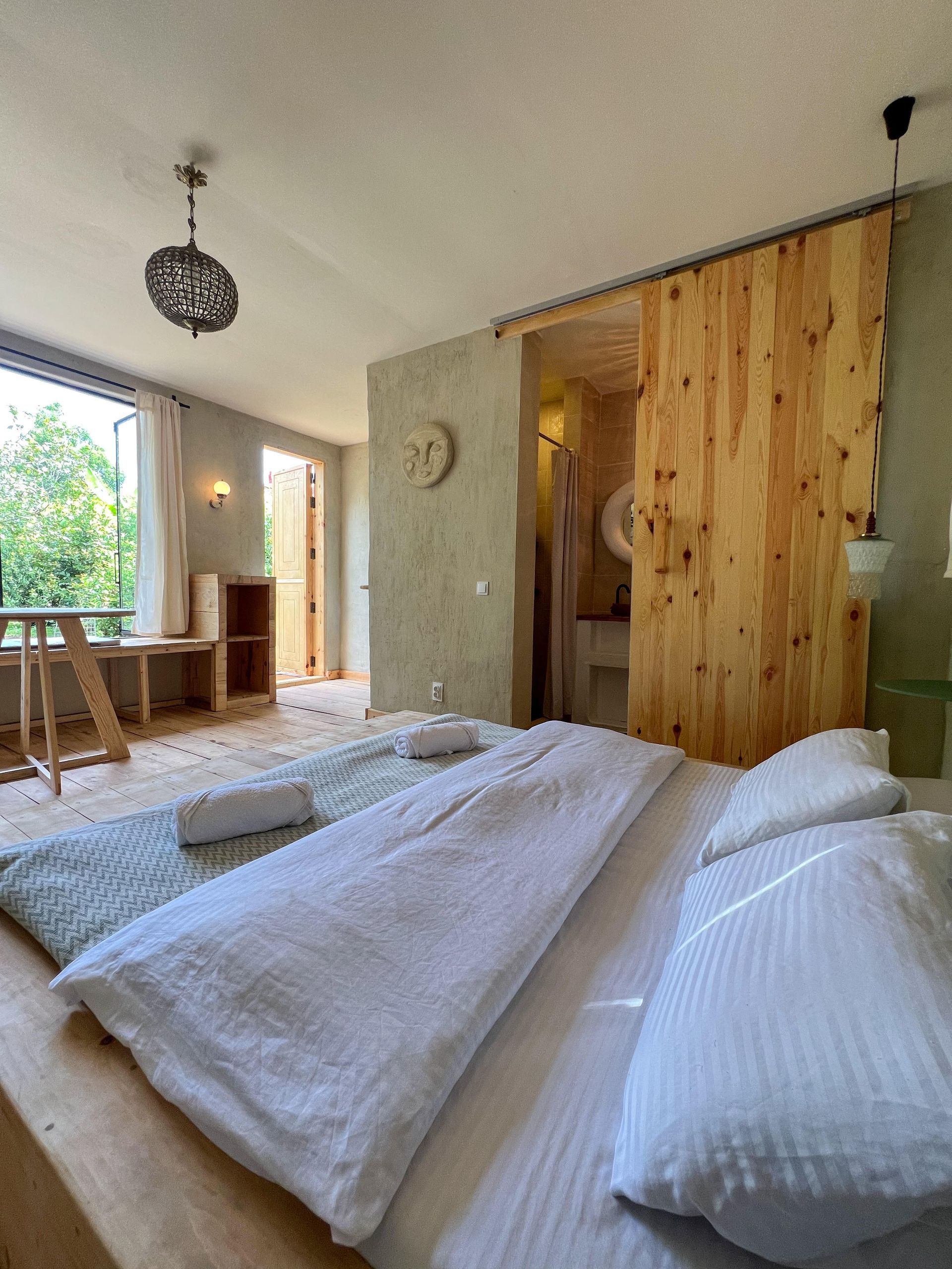 A rustic bedroom featuring a bed with white linens, textured earth-toned walls, and a large natural wood sliding door.