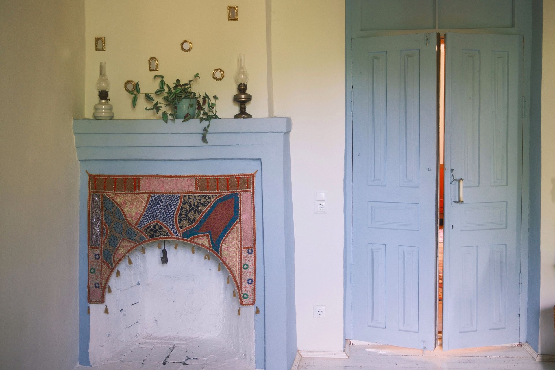 A room features a light blue fireplace with a patterned fabric hearth cover and a light blue double door beside it.